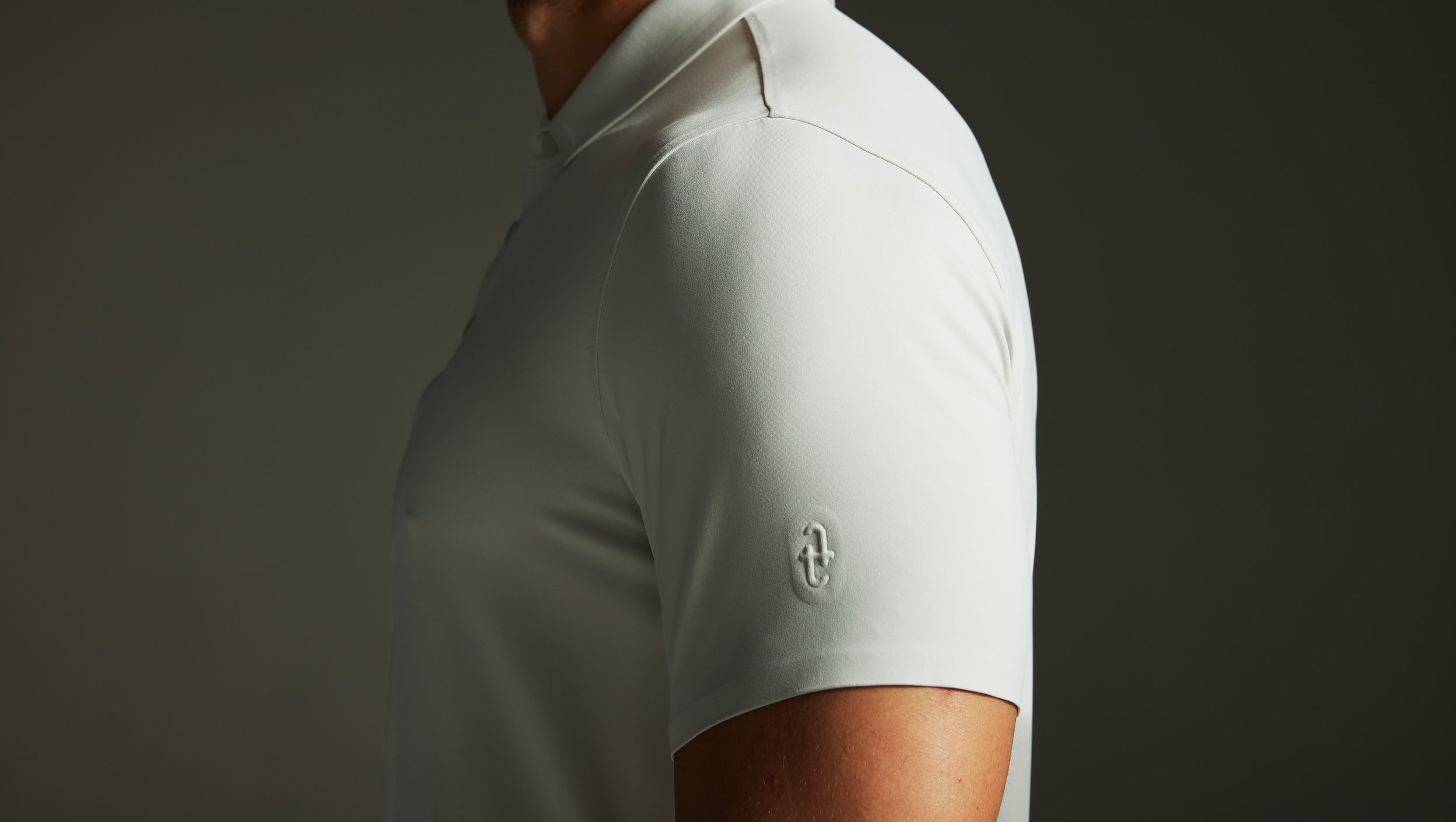Grey polo shirt with a techtee logo on the sleeve against a dark background