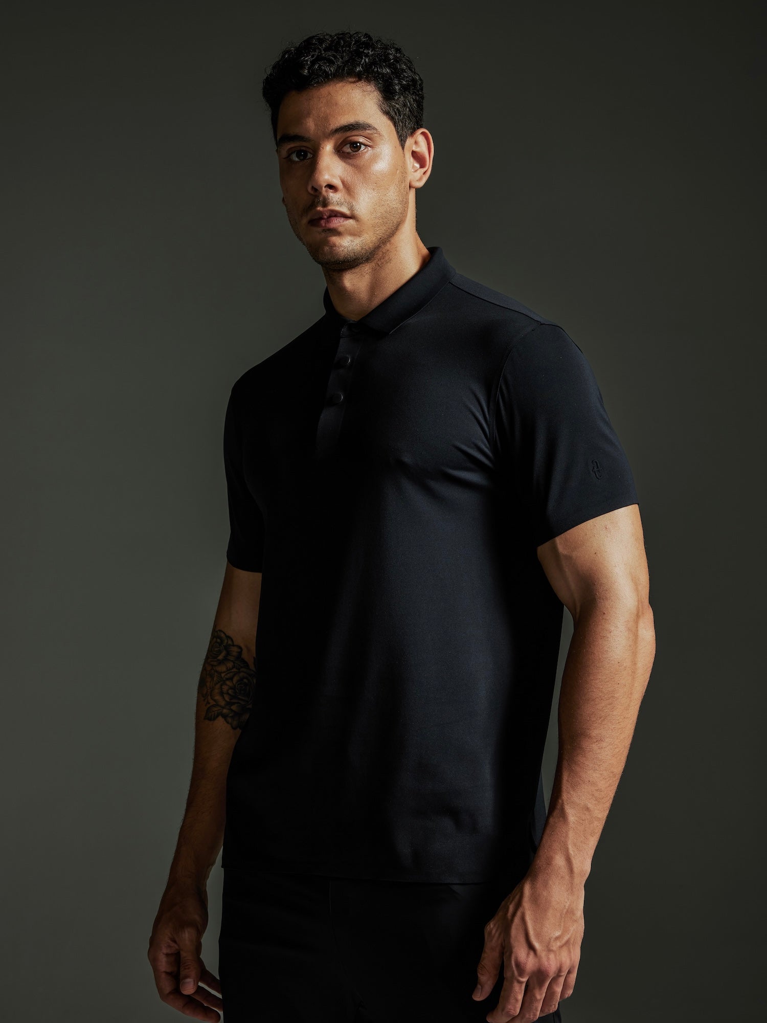 Man wearing the TECHTEE black polo shirt against a dark background