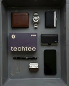 Collection of men's accessories including a wallet, watch, cards, phone, and earbuds on a gray surface with 'techtee' branding.