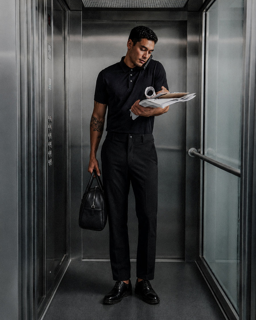 Man in an all black outfit holding a bag and files in an elevator